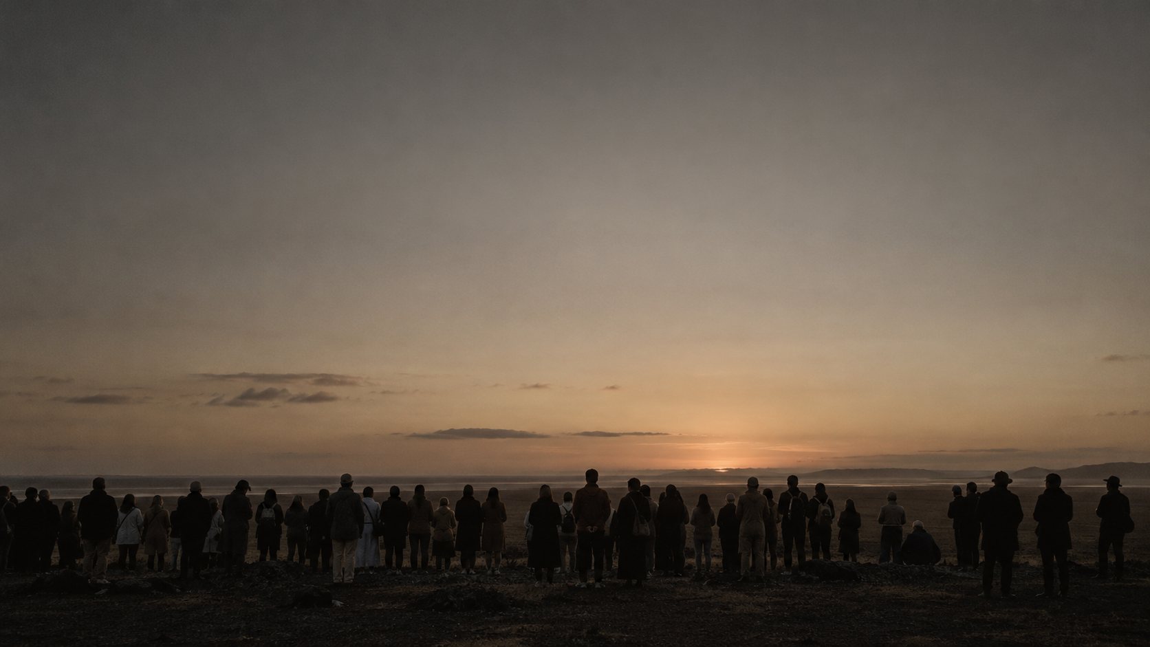 A distant crowd seen from behind at dusk, facing the same open horizon.